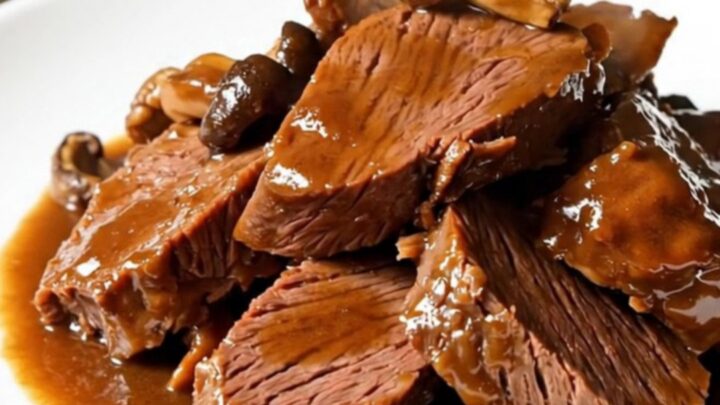 A close-up of tender braised beef and porcini mushrooms served on a white plate.