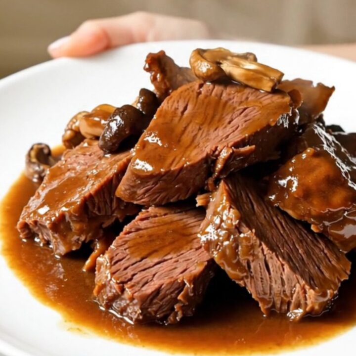 A close-up of tender braised beef and porcini mushrooms served on a white plate.