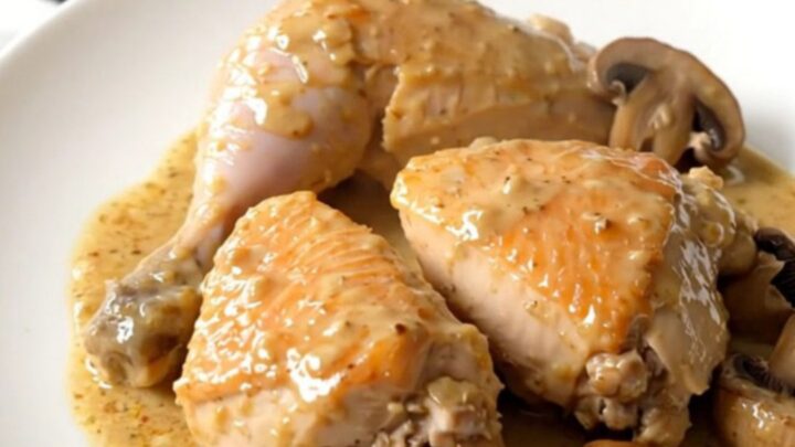 A close-up of slow cooker chicken suprême with mushrooms in a creamy sauce on a white plate.