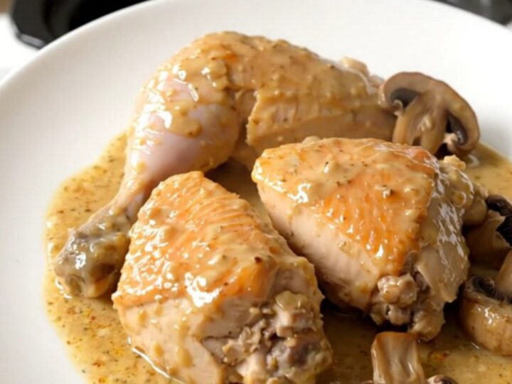 A close-up of slow cooker chicken suprême with mushrooms in a creamy sauce on a white plate.