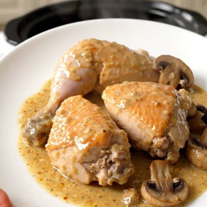 A close-up of slow cooker chicken suprême with mushrooms in a creamy sauce on a white plate.