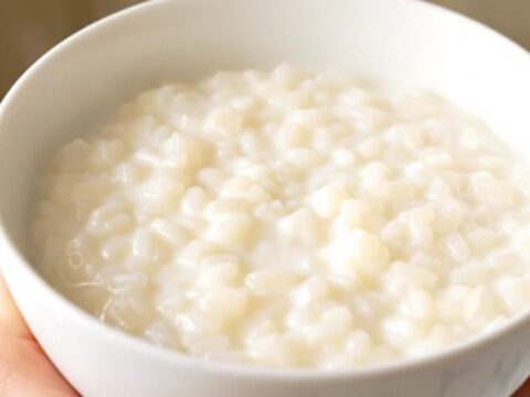 A close-up view of a white ceramic bowl filled with creamy orange zest rice pudding, showing a smooth, glossy texture.