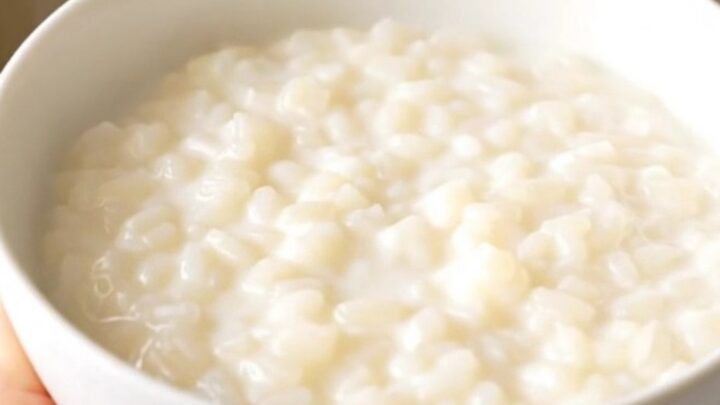 A close-up view of a white ceramic bowl filled with creamy orange zest rice pudding, showing a smooth, glossy texture.