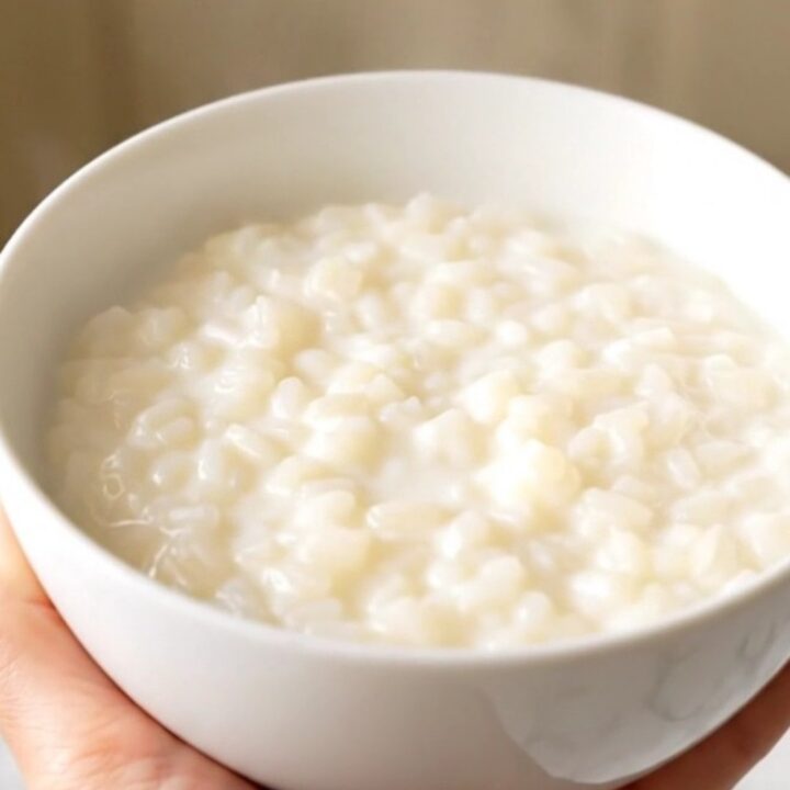 A close-up view of a white ceramic bowl filled with creamy orange zest rice pudding, showing a smooth, glossy texture.