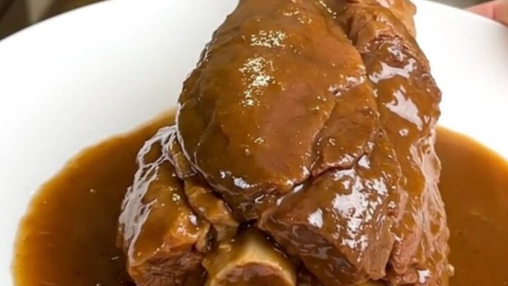 Jarret de veau fondant servi dans une assiette blanche avec une sauce brillante.