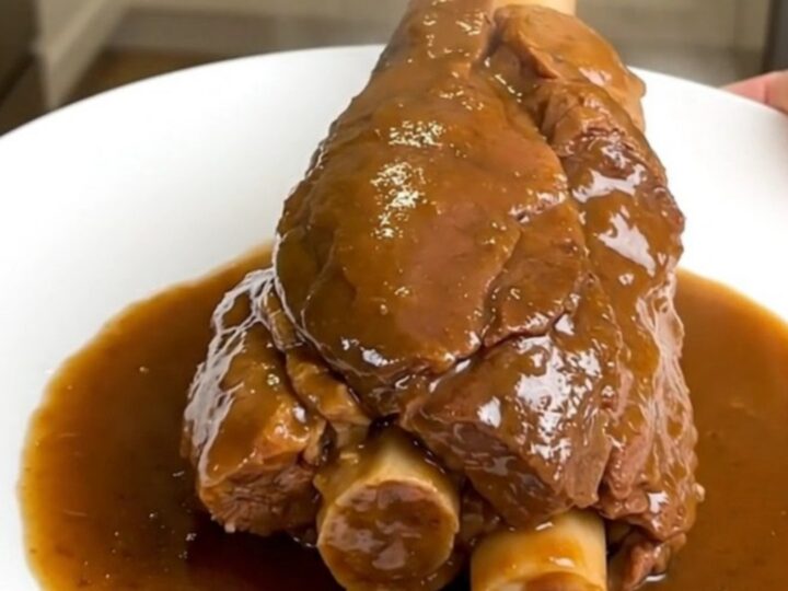 Jarret de veau fondant servi dans une assiette blanche avec une sauce brillante.