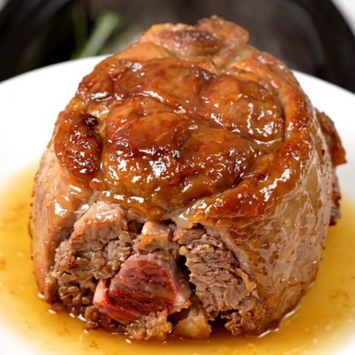 Succulent slow-cooked pork collar served on a white plate with fresh rosemary.