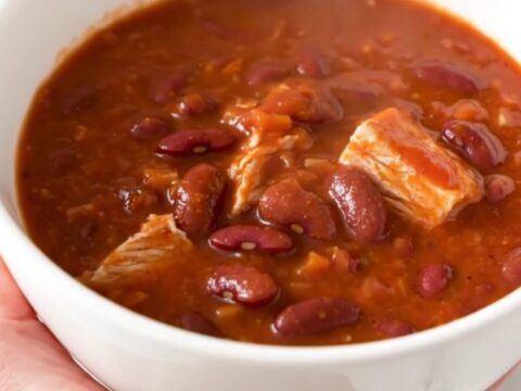A steaming bowl of turkey chili with kidney beans and a rich tomato sauce, served in a white bowl.