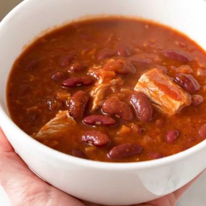 A steaming bowl of turkey chili with kidney beans and a rich tomato sauce, served in a white bowl.