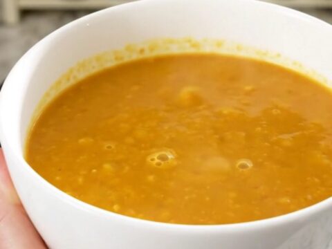 A bowl of creamy, bright orange butternut squash soup in a white bowl on a quartz countertop.