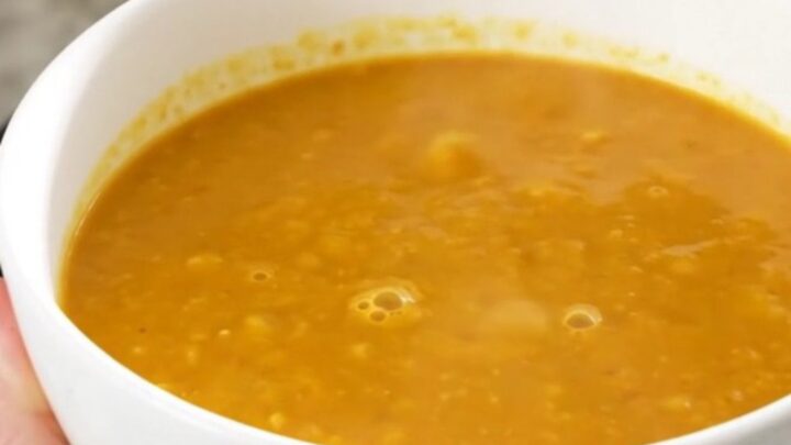 A bowl of creamy, bright orange butternut squash soup in a white bowl on a quartz countertop.