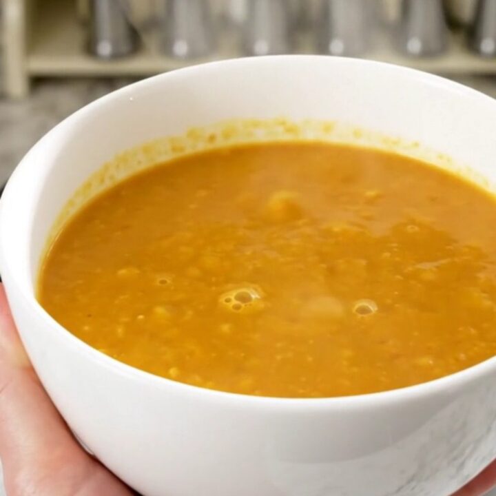 A bowl of creamy, bright orange butternut squash soup in a white bowl on a quartz countertop.
