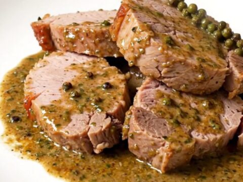 A succulent sliced pork tenderloin topped with a glossy, creamy green peppercorn sauce on a white plate.