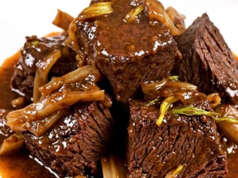 A close-up of glossy, braised beef cheeks and soft fennel slices served on a white plate.