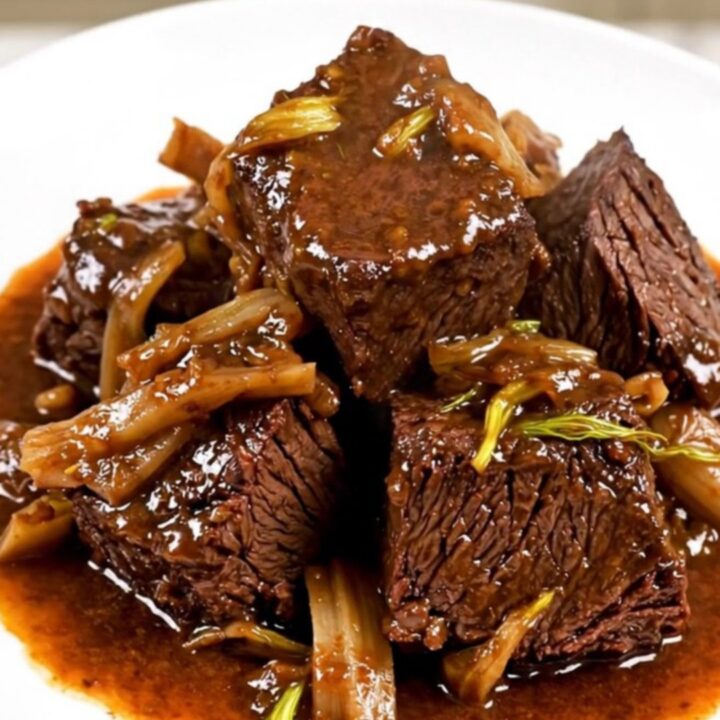 A close-up of glossy, braised beef cheeks and soft fennel slices served on a white plate.