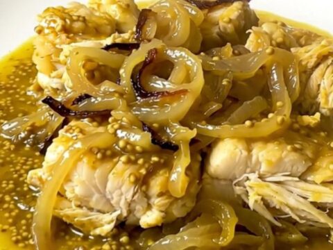 A top-down view of raw white fish fillets, sliced onions, and sauce inside a black oval slow cooker on a speckled countertop.