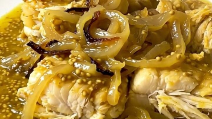 A top-down view of raw white fish fillets, sliced onions, and sauce inside a black oval slow cooker on a speckled countertop.