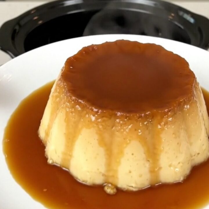 A top-down view of a black slow cooker insert showing the layered ingredients for a coffee caramel flan.
