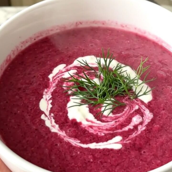 A steaming white bowl of vibrant magenta beet and potato velouté with a swirl of cream and fresh dill.