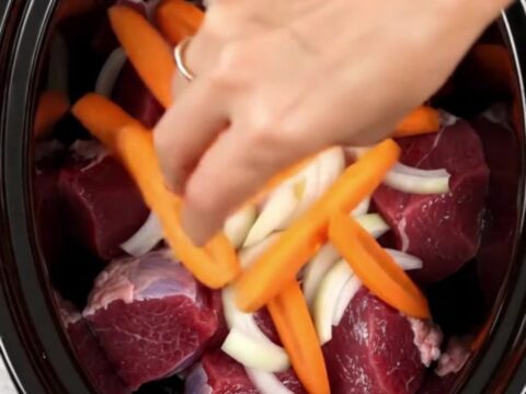 A top-down view of tender braised veal with carrots and cumin in a slow cooker.