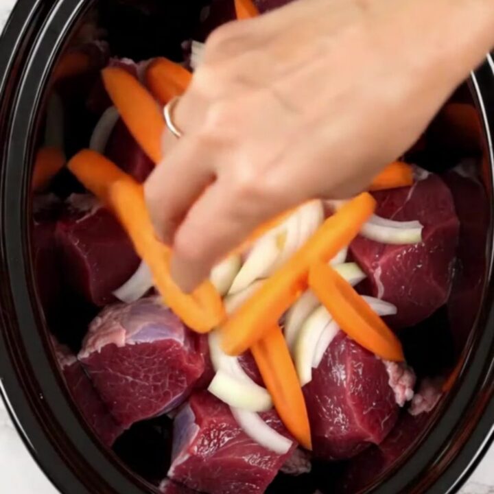 A top-down view of tender braised veal with carrots and cumin in a slow cooker.