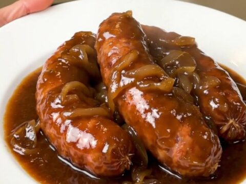 A rustic plate of slow-cooked sausages coated in a rich, glossy red wine and onion gravy.