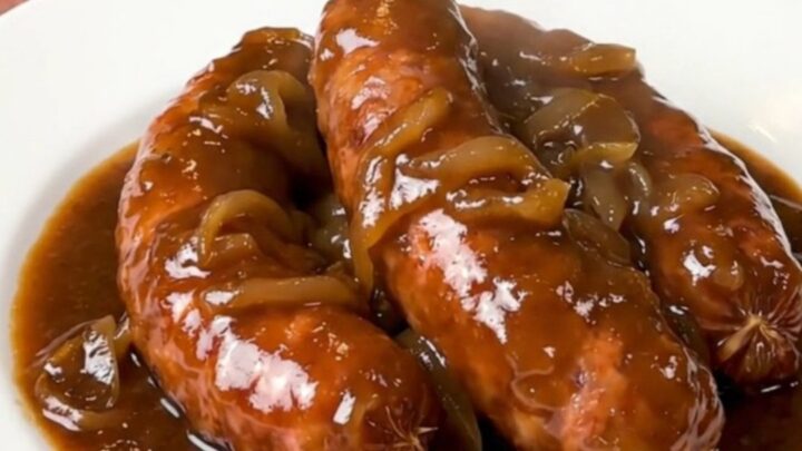 A rustic plate of slow-cooked sausages coated in a rich, glossy red wine and onion gravy.