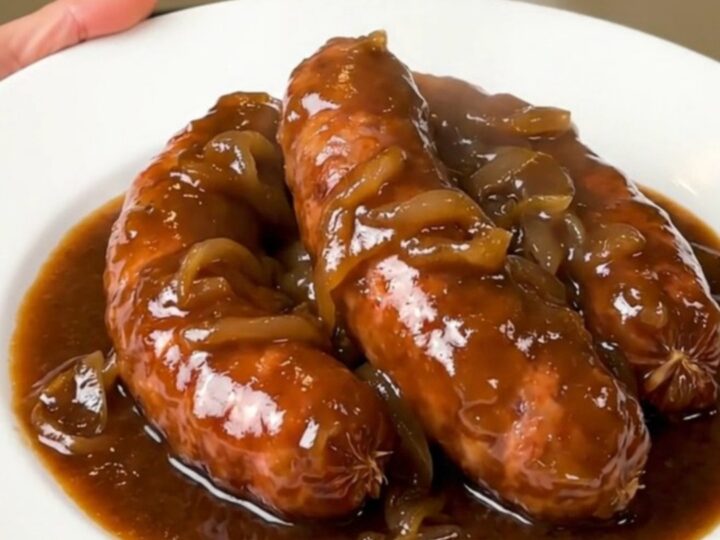 A rustic plate of slow-cooked sausages coated in a rich, glossy red wine and onion gravy.