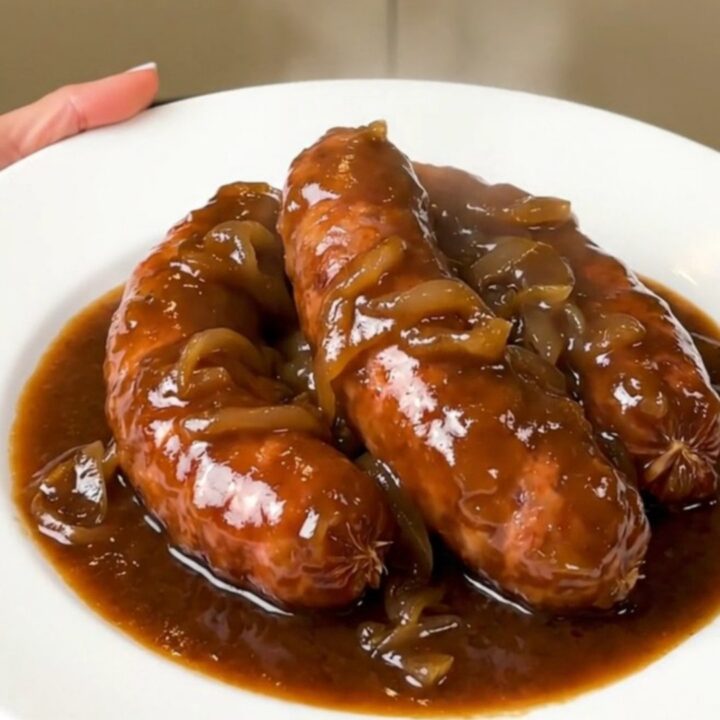 A rustic plate of slow-cooked sausages coated in a rich, glossy red wine and onion gravy.