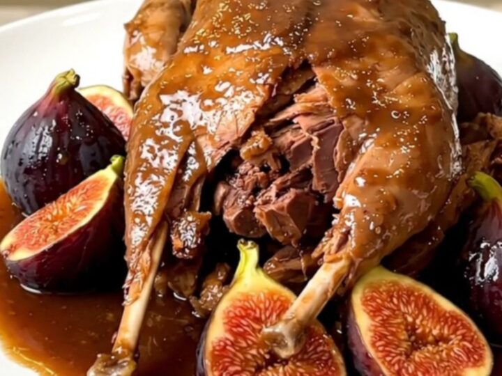 A rustic slow cooker filled with guinea fowl, fresh fig halves, and sliced shallots in a rich port wine sauce.