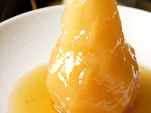 Four whole peeled pears standing upright in a black slow cooker, ready to be poached.