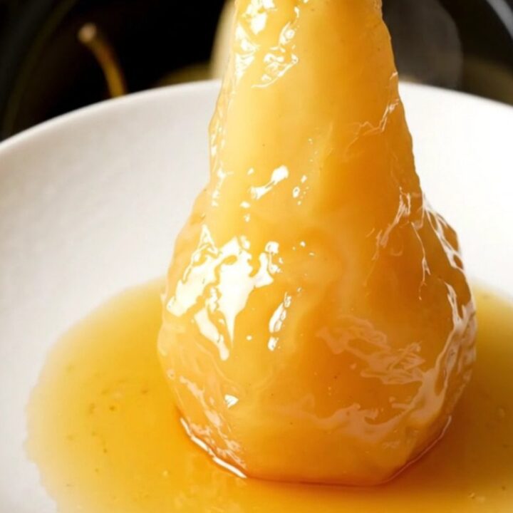 Four whole peeled pears standing upright in a black slow cooker, ready to be poached.