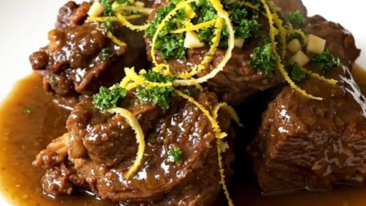 A close-up of tender osso buco served on a white plate, topped with a vibrant green gremolata.