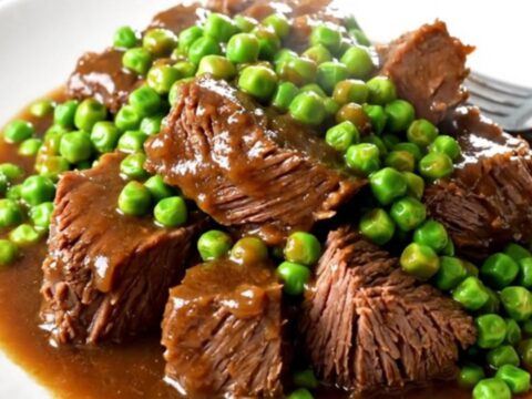 Bœuf braisé fondant servi dans une assiette blanche avec des carottes et des petits pois.