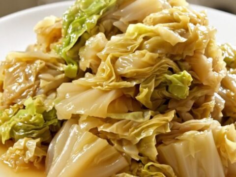 A top-down view of a slow cooker filled with layers of sliced onions and shredded white cabbage.