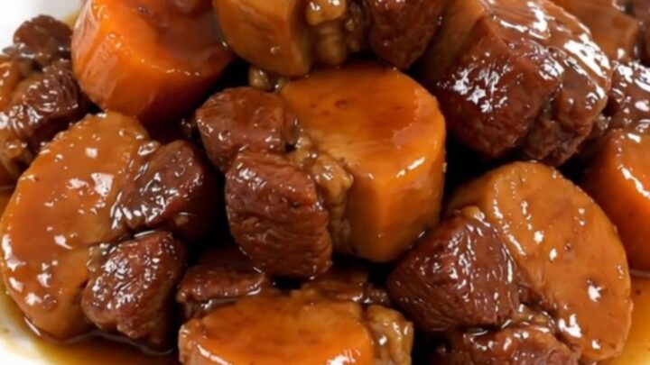 A white plate featuring tender, glazed pork cheeks and soft carrot rounds, steaming slightly.