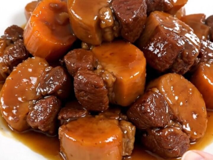 A white plate featuring tender, glazed pork cheeks and soft carrot rounds, steaming slightly.