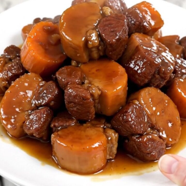 A white plate featuring tender, glazed pork cheeks and soft carrot rounds, steaming slightly.