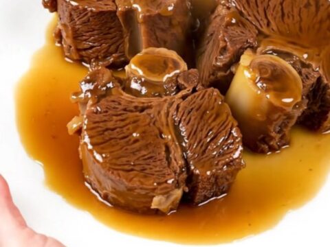 A close-up of tender, glossy beef cheeks in a citrus glaze served on a white plate.