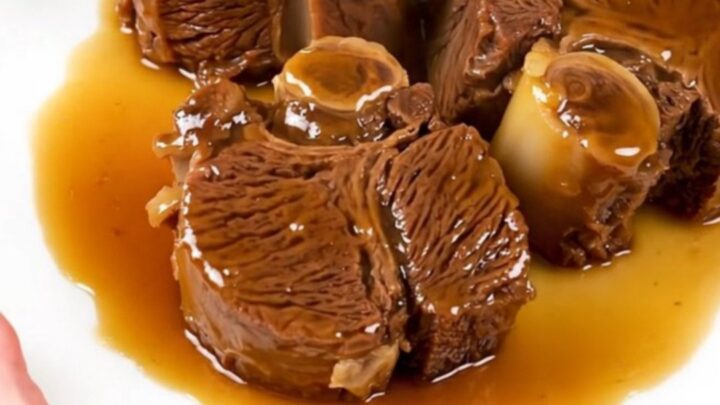 A close-up of tender, glossy beef cheeks in a citrus glaze served on a white plate.