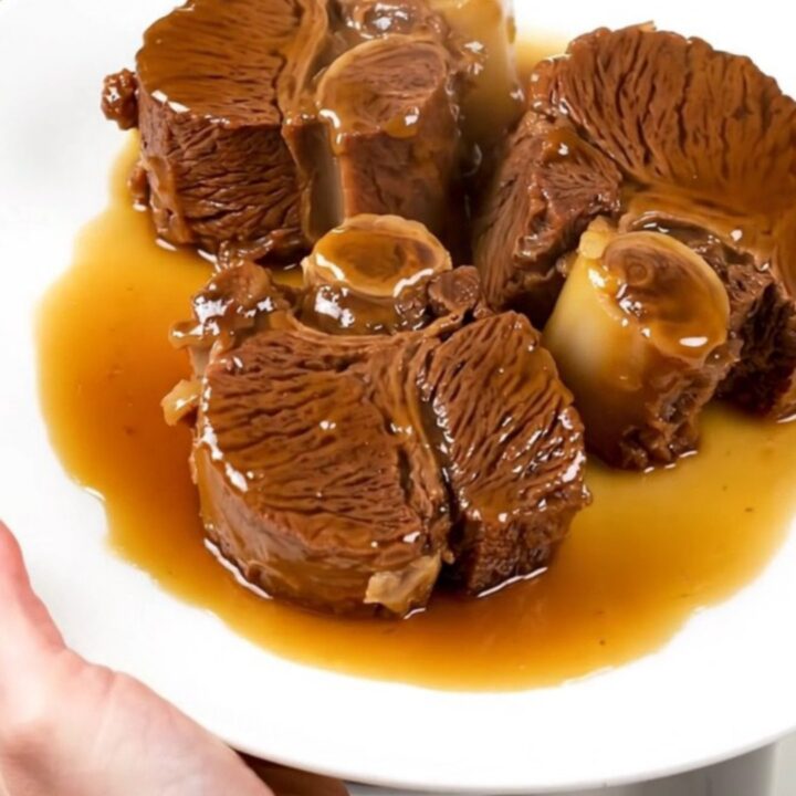 A close-up of tender, glossy beef cheeks in a citrus glaze served on a white plate.