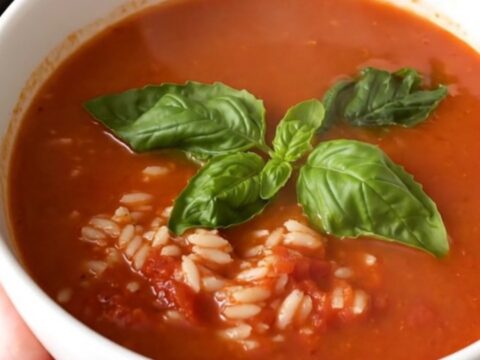Bol de soupe de tomates au riz rougeoyante et brillante, garni de feuilles de basilic frais.