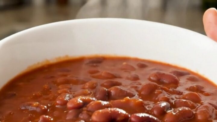 A white bowl filled with slow-cooked red beans and sliced smoked sausage in a rich tomato sauce.