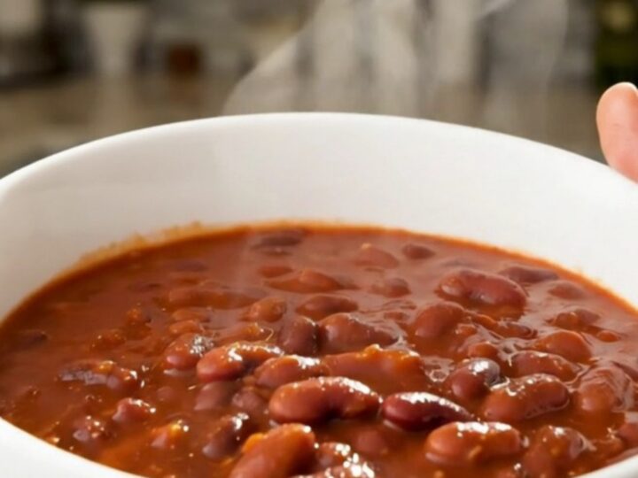 A white bowl filled with slow-cooked red beans and sliced smoked sausage in a rich tomato sauce.