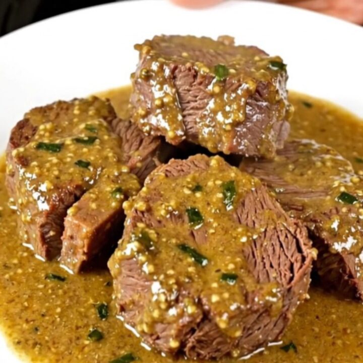 Slow cooked beef chuck slices served on a white plate with creamy tarragon mustard sauce.