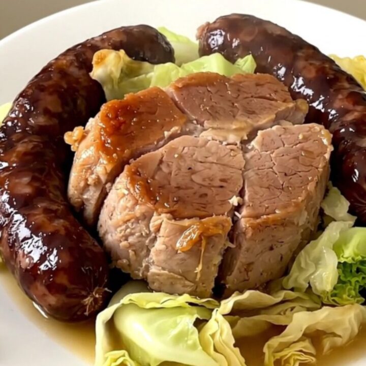 A top-down view of a slow cooker filled with pork shoulder, sliced sausages, and shredded cabbage.