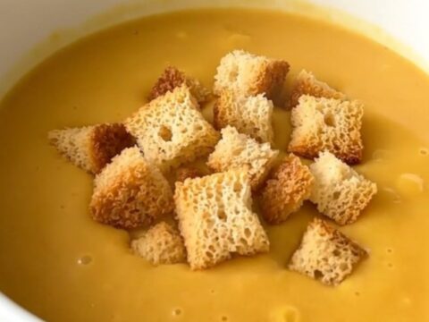 A steaming bowl of creamy orange butternut squash velouté garnished with golden croutons.