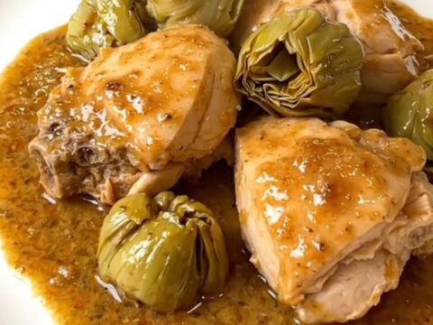 A white plate holding slow-cooked chicken thighs and Jerusalem artichokes in a creamy sauce.