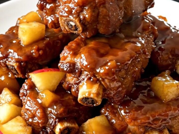 A close-up of tender, glossy pork ribs topped with soft, caramelized apple pieces in a slow cooker.