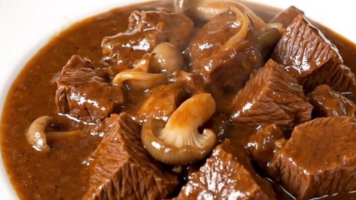 A close-up of a slow cooker beef stew with tender beef cubes and pleurotus mushrooms in a rich red wine sauce.